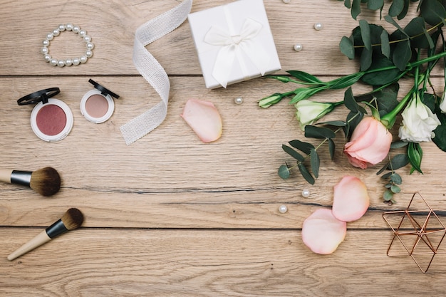 Make-up kwast; compact gezichtspoeder; parels; geschenkdoos; roos en eustoma bloemen op houten bureau