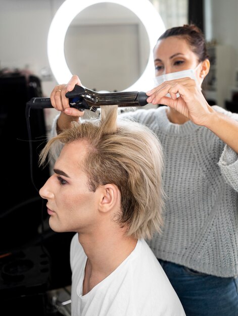 Make-up man met behulp van stijltang op zijn haar