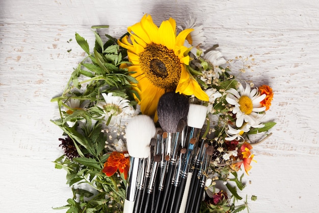Make-up penselen op een stapel wilde bloemen op houten achtergrond