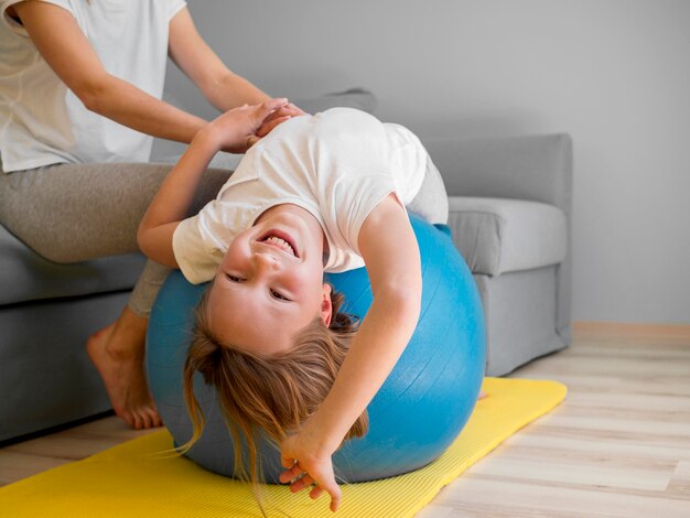 Mam helpt meisje om op bal te trainen