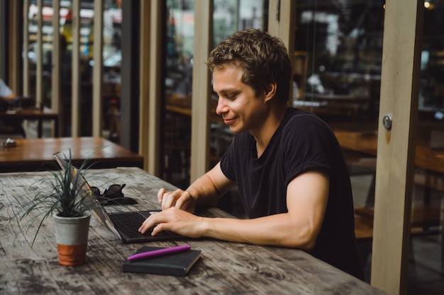 man aan het werk met een laptop in een café op een houten tafel