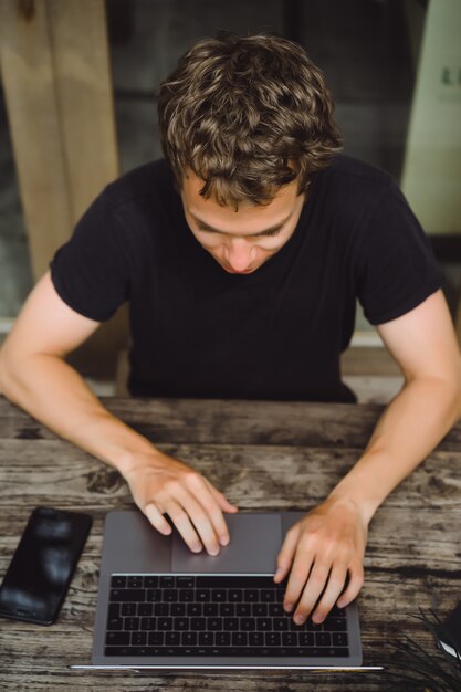 man aan het werk met een laptop in een café op een houten tafel