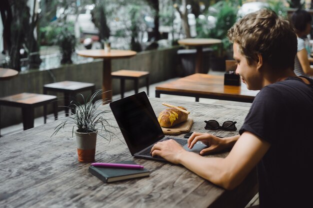 man aan het werk met een laptop in een café op een houten tafel