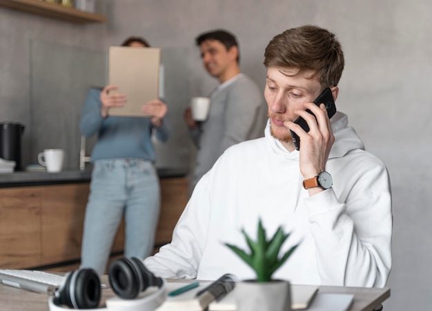 Gratis foto man aan het werk op het gebied van media praten over smartphone terwijl collega's kijken naar tablet