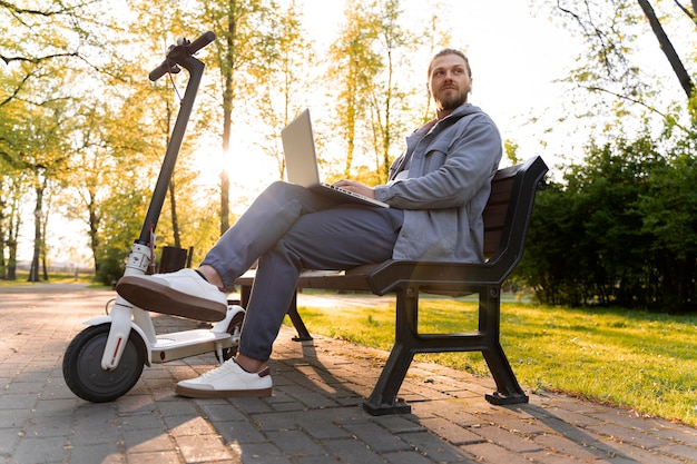 Man aan het werk op zijn laptop naast zijn scooter