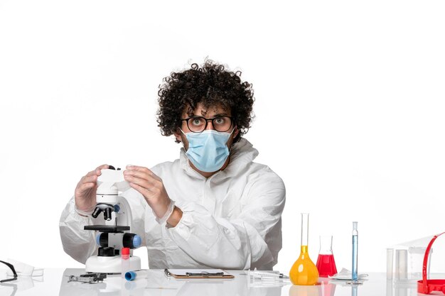 man arts in beschermend pak en masker werken met microscoop op wit