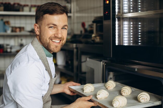 Man bakker zet croissantdeeg in de oven