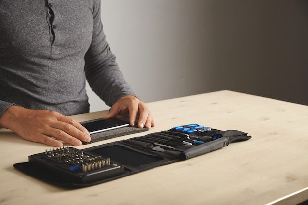 Man bereidt zich voor om de telefoon thuis te demonteren met zijn persoonlijke draagbare gereedschapsset op tafel. Ruimte voor uw tekst aan de rechterkant