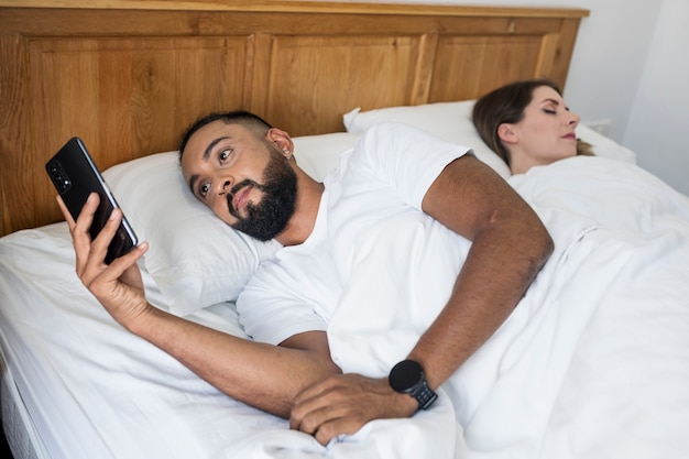 Man checkt zijn telefoon in bed naast zijn vrouw
