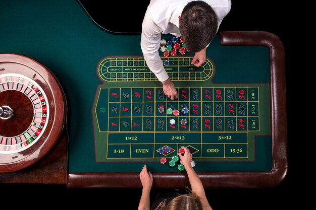 Man croupier en vrouw spelen roulette aan de tafel in het casino. Bovenaanzicht op een groene roulettetafel met een meetlint.