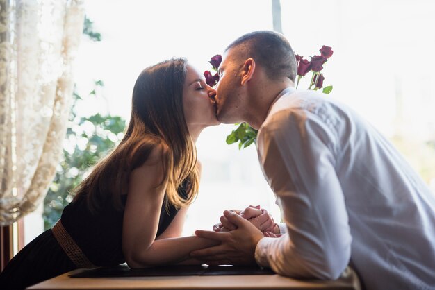 Man die aantrekkelijke vrouw kussen dichtbij bloemen en venster