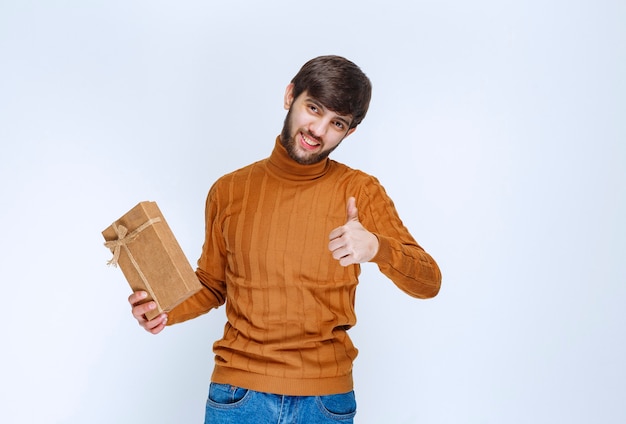 Man die een kartonnen geschenkdoos vasthoudt en een teken van plezier toont.