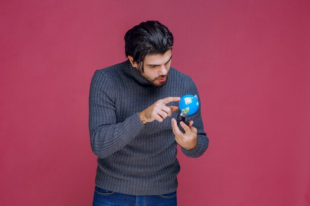 Man die een mini-wereldbol vasthoudt en daar een locatie probeert te vinden.