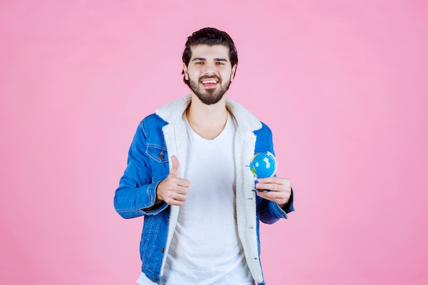 Man die een mini-wereldbol vasthoudt en een teken van plezier toont