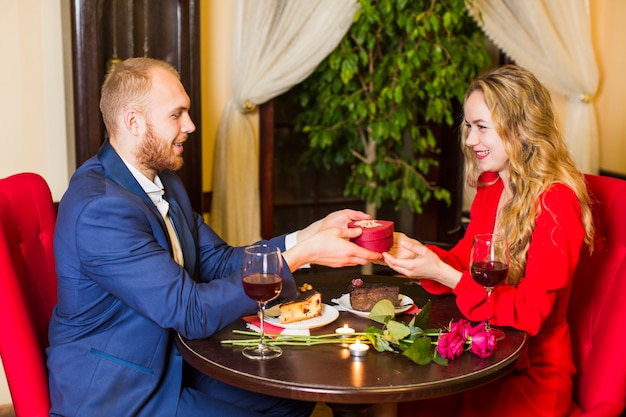 Gratis foto man die geschenkdoos in hartvorm geeft aan vrouw aan tafel