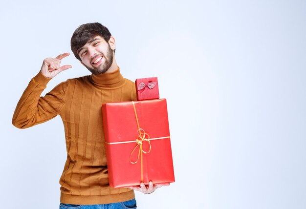 Man die grote en kleine rode geschenkdozen vasthoudt en de maat in de hand laat zien.