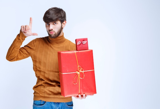 Gratis foto man die grote en kleine rode geschenkdozen vasthoudt en de maat in de hand laat zien.