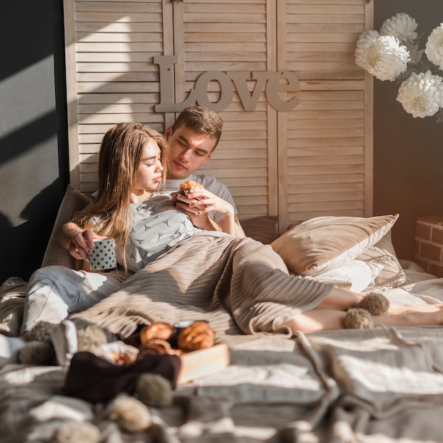 Man die met haar vriendin voedende croissant aan haar op bed liggen