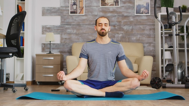 Man die mindfulness beoefent op yogamat in een gezellige woonkamer.