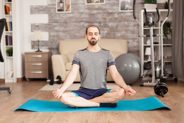 Man die mindfulness beoefent op yogamat op mat tijdens wereldwijde isolatie. Zwitserse bal op de achtergrond.