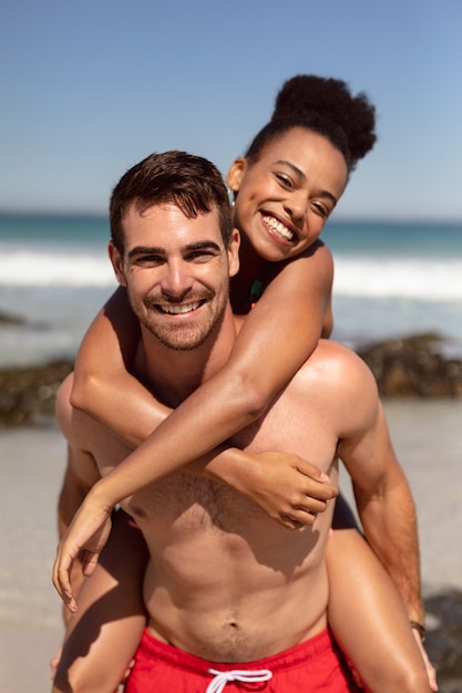 Man die op de rug aan vrouw op strand in de zonneschijn geeft