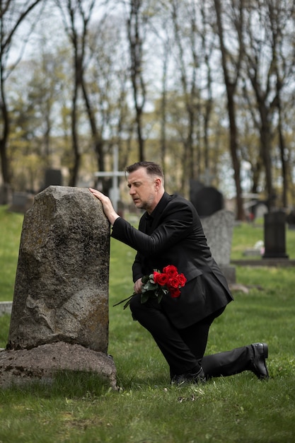 Gratis foto man die respect betuigt aan een grafsteen op de begraafplaats