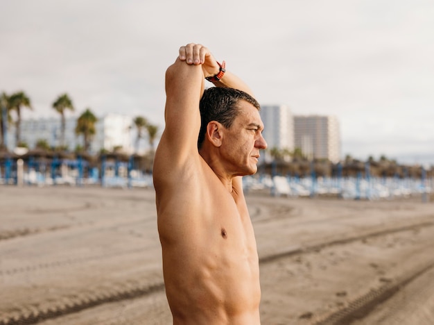 Gratis foto man die zich uitstrekt op het strand zijaanzicht