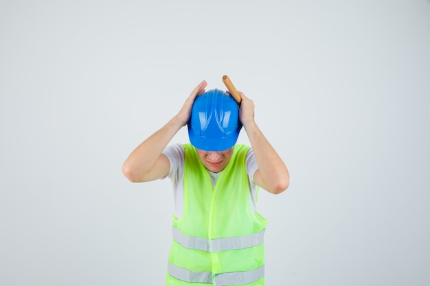 Man die zijn handen tegen de oren drukt en een hamer vasthoudt in een bouwuniform