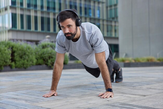 man doet plankoefening demonstreert uithoudingsvermogen poseert in de stad luistert muziek in koptelefoon maakt krachttraining traint lichaam doet push-ups