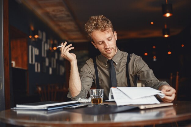 Man drinkt whisky. Zakenman leest documenten. Regisseur in een overhemd en bretels.