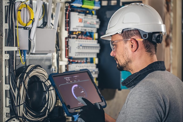 Man een elektrotechnicus die in een schakelbord met zekeringen werkt, gebruikt een tablet