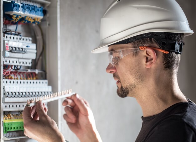 Man, een elektrotechnicus die in een schakelbord met zekeringen werkt. Installatie en aansluiting van elektrische apparatuur.