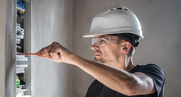 Man, een elektrotechnicus die in een schakelbord met zekeringen werkt. Installatie en aansluiting van elektrische apparatuur.