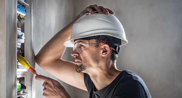 Man, een elektrotechnicus die werkt in een schakelbord met zekeringen. Installatie en aansluiting van elektrische apparatuur.