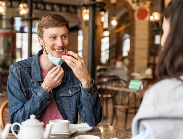 Man eet wat cake in het restaurant terwijl hij zijn gezichtsmasker op zijn kin draagt