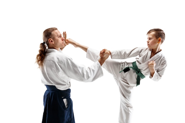 Man en tienerjongen die vechten bij Aikido-opleiding in vechtsportschool. Gezonde levensstijl en sportconcept. Vechters in witte kimono op witte muur. Karatemannen met geconcentreerde gezichten in uniform.