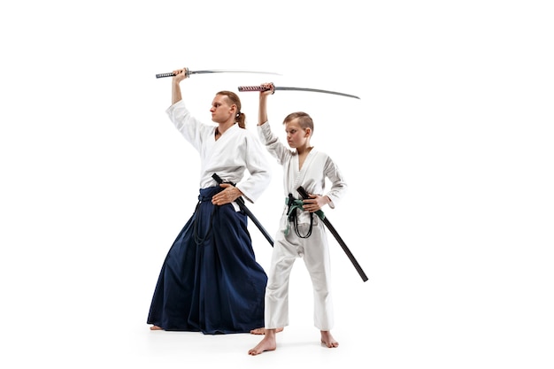 Man en tienerjongen die vechten bij Aikido-opleiding in vechtsportschool. Gezonde levensstijl en sportconcept. Vechters in witte kimono op witte muur. Karatemannen met geconcentreerde gezichten in uniform.