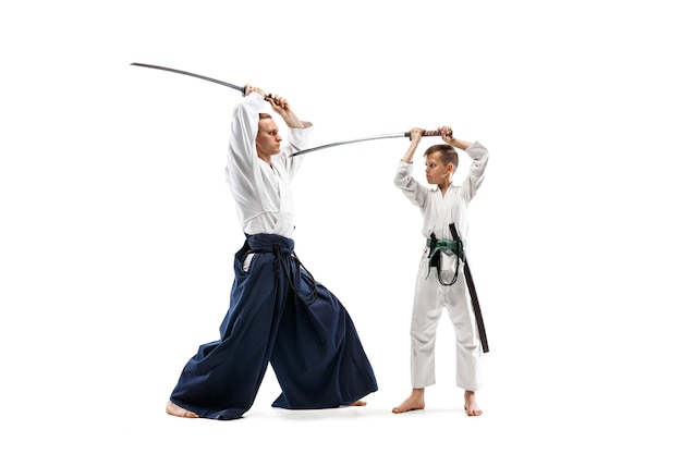 Man en tienerjongen die vechten bij Aikido-opleiding in vechtsportschool. Gezonde levensstijl en sportconcept. Vechters in witte kimono op witte muur. Karatemannen met geconcentreerde gezichten in uniform.