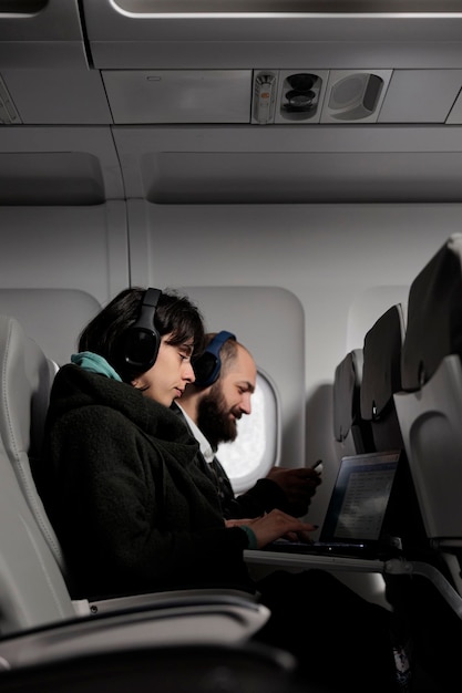 Gratis foto man en vrouw die laptop en smartphone gebruiken op vliegtuigvlucht, wachtend om op vakantievakantie aan te komen. aantal passagiers die aan apparaten werken en reizen met een internationale luchtvaartmaatschappij.
