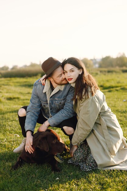 Man en vrouw in modekleren rustend op een natuur met hun labrador. Man met jas en een zwarte hoed en vrouwenjas