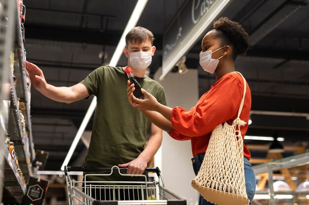 Man en vrouw met medische maskers boodschappen doen met winkelwagentje