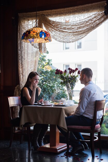 Man en vrouw zitten aan tafel met desserts, drankjes en bloemen in café