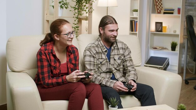 Man en vrouw zitten op de bank en spelen videogames met behulp van een draadloze controller.