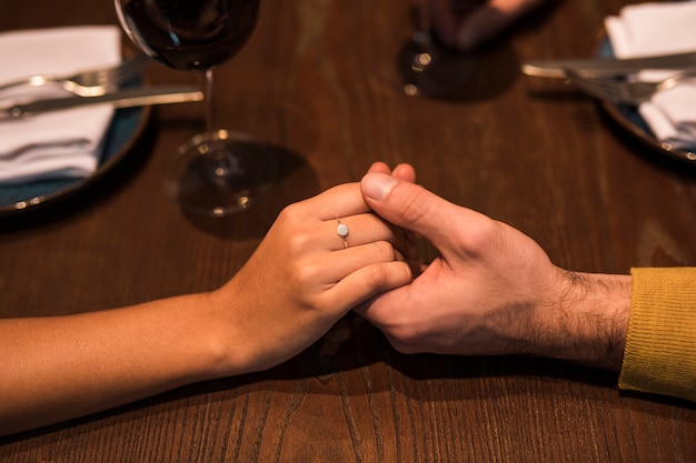 Man en vrouwenholdingshanden bij lijst met platen en glazen wijn in restaurant