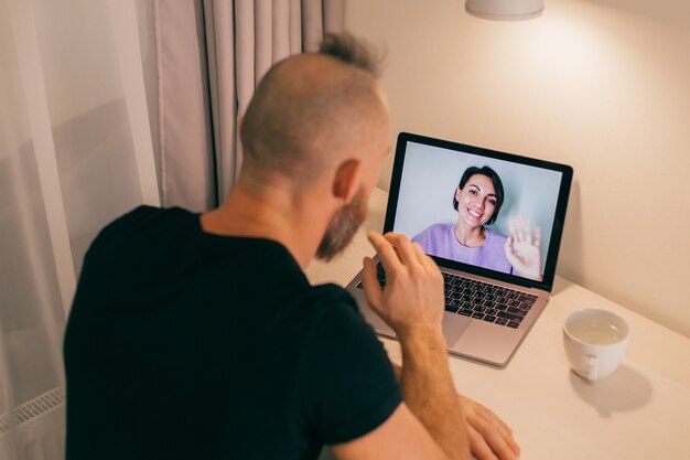 Man face-time thuis, de vriendin van zijn vriend, vrouw, vriendin bellen vanaf laptop in de slaapkamer.