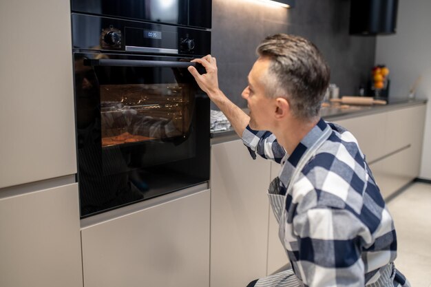 Man gehurkt kijken naar bakken in elektrische oven