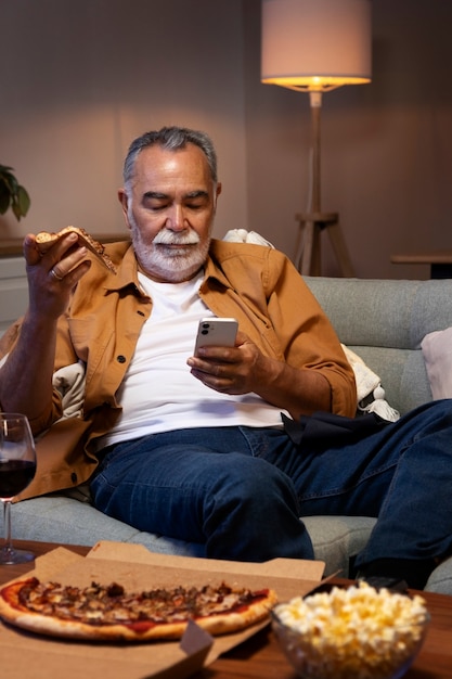 Man geniet van wat te eten terwijl hij alleen thuis is en smartphone gebruikt