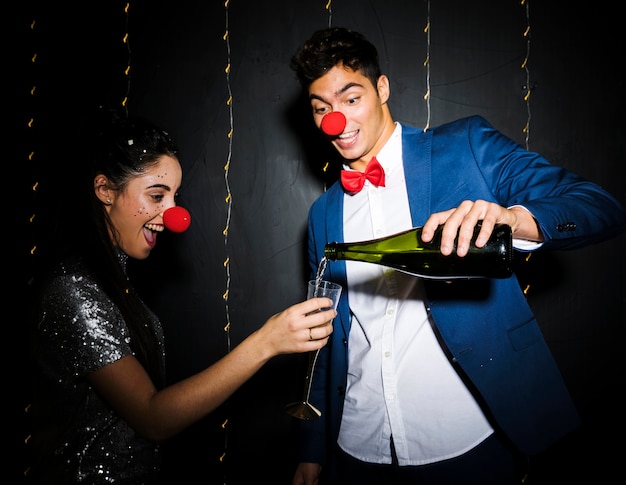 Man gieten drankje in glas van lachende jonge vrouw in grappige neuzen