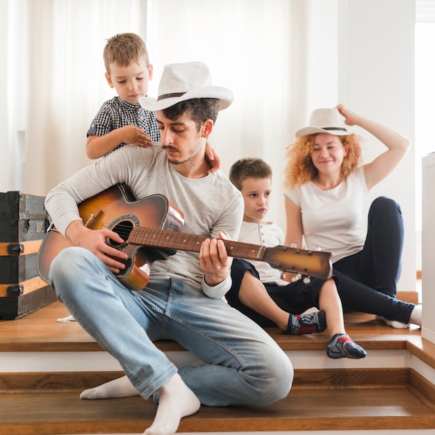 Gratis foto man gitaar spelen voor zijn familie thuis