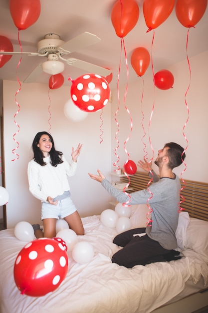 Man glimlachend terwijl zijn vriendin kijkt naar de kamer vol met rode ballonnen